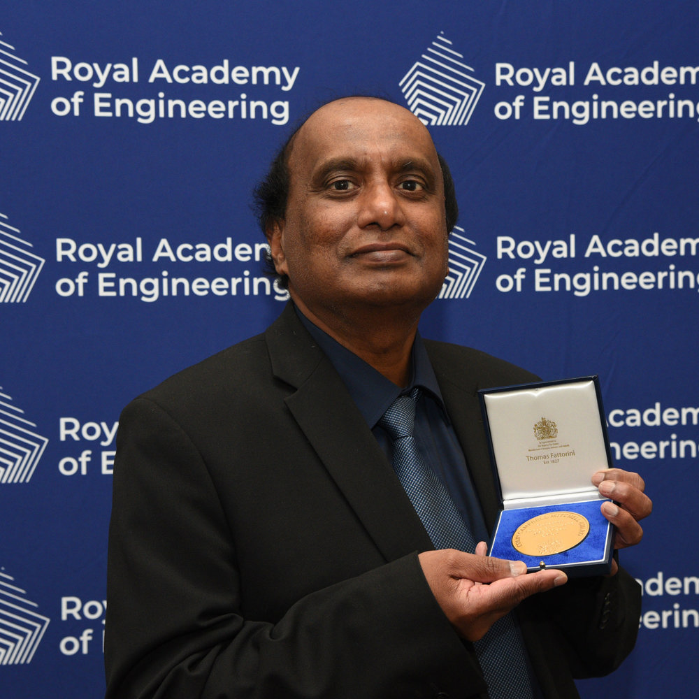 Professor Mohan Edirisinghe OBE FREng stood holding the Colin Campbell Mitchell Award in front of a blue screen with the Royal Academy of Engineering logo