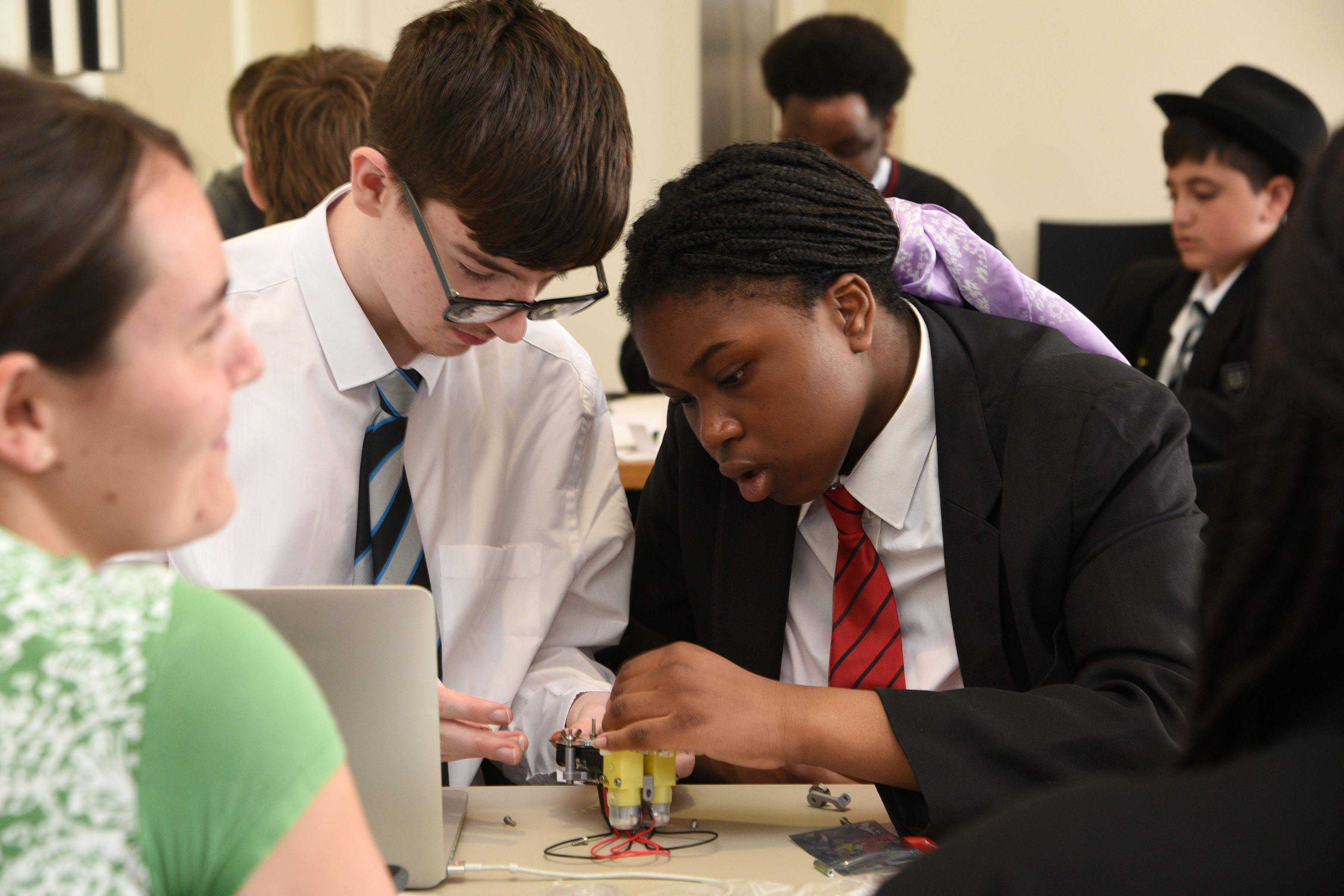 School students inspect small engineering equipment at a table.