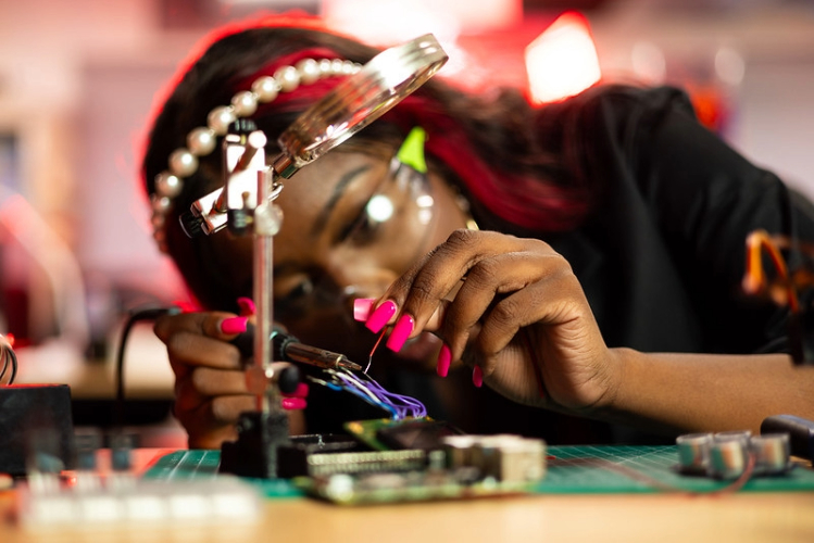 A young women with pink nails works on an electrical circuit.