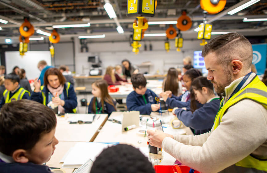 A group of children and adults in a design and technology classroom.